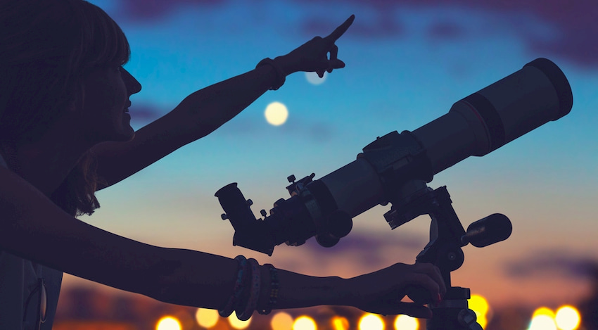 a woman looks and points through a telescope on the lawn of the Griffith Observatory in Los Angeles, California