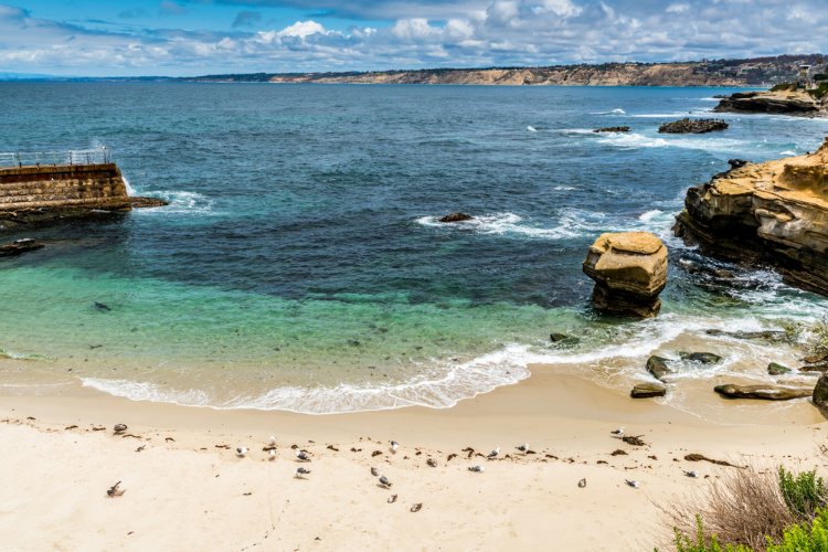Picture of La Jolla Cove with large rocks, blue water, and white sand 