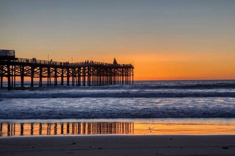 Picture of sunset at Mission Beach with the boardwalk and the water darkened in front of the sky 