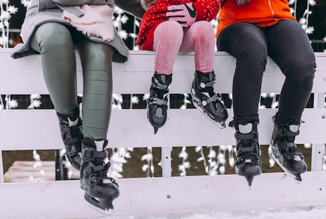 two adults and a child sit on a fence around a skate rink while wearing ice skates