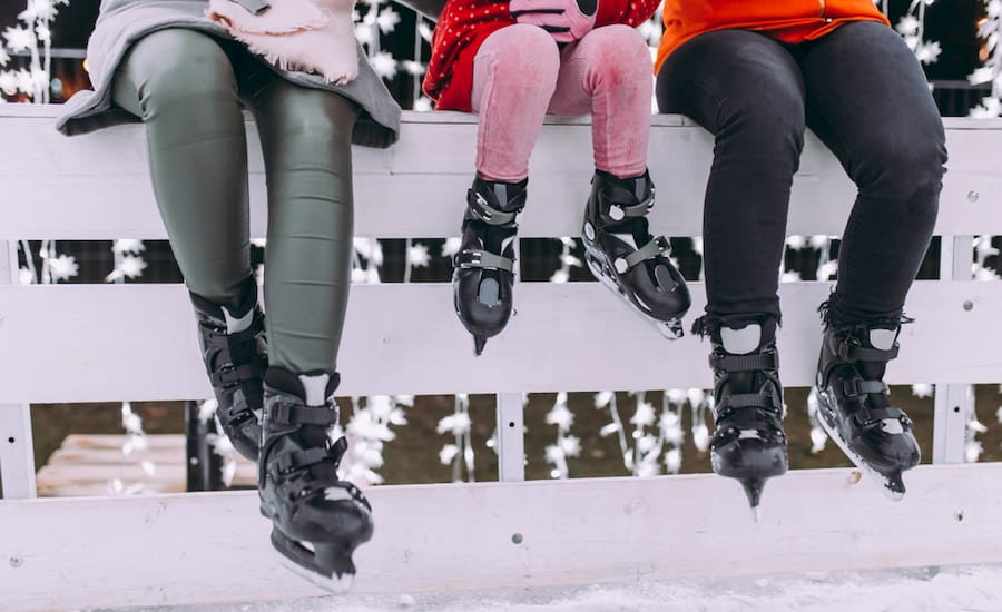 two adults and a child sit on a fence around a skate rink while wearing ice skates