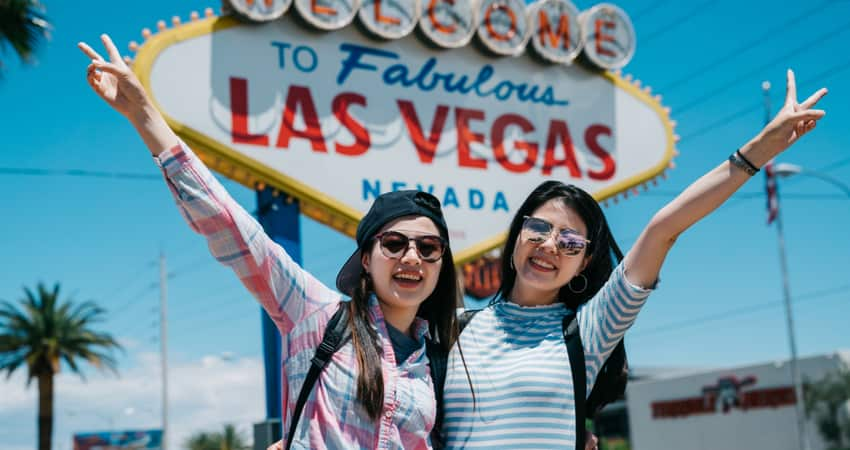 two women posing with the peace hand sign in front of the Las Vegas Sign