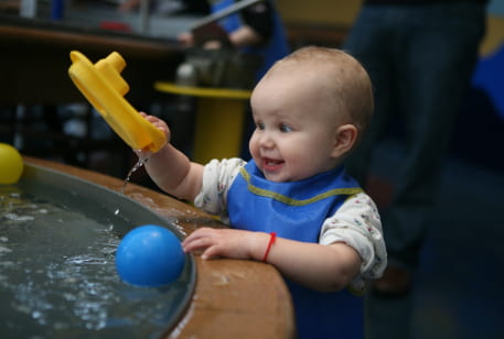 a small toddler plays at a water table in a children's museum