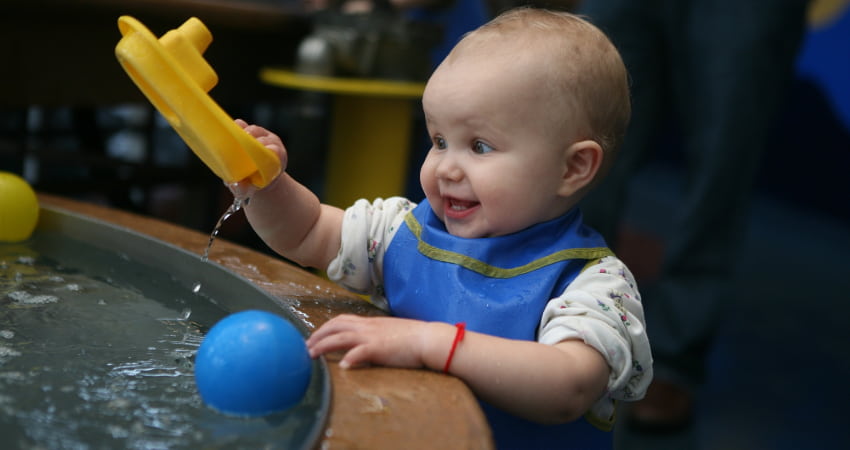 a small toddler plays at a water table in a children's museum