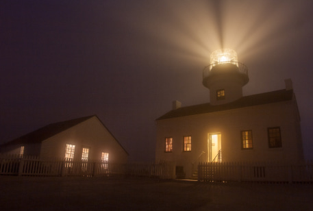 The Old Poma Lighthouse on a foggy night, beacon shining into the sky