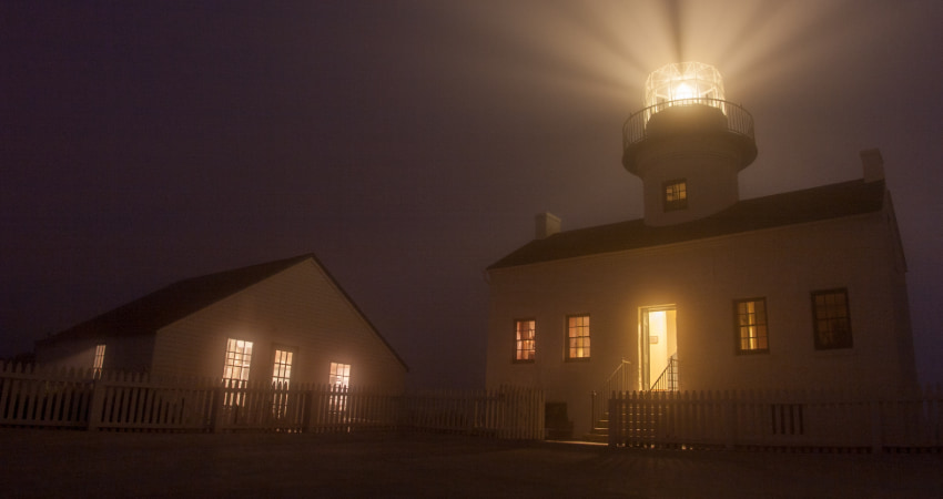 The Old Poma Lighthouse on a foggy night, beacon shining into the sky