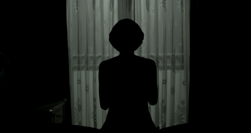 The silhouette of a woman standing in front of a curtained window