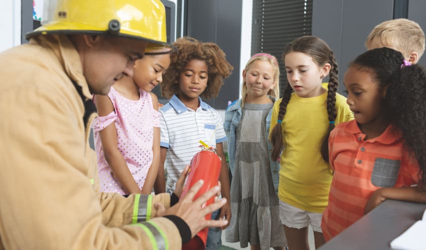 A firefighter shows a fire extinguisher to a class of curious children