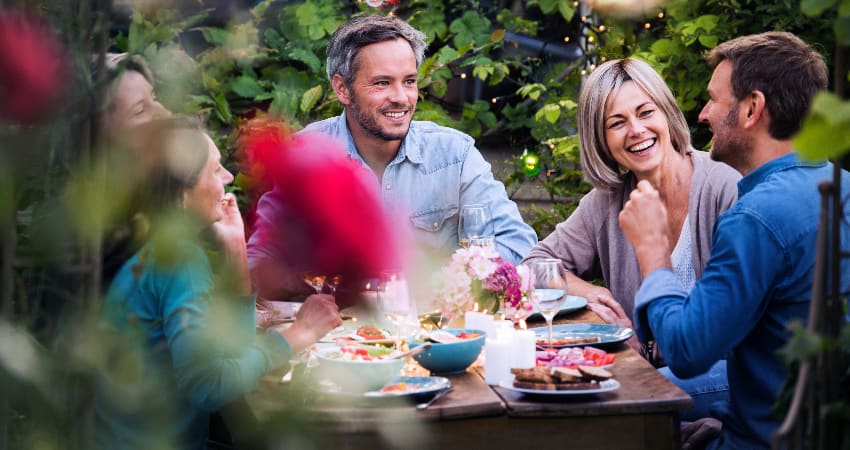 A group of dinner guests eat food in a garden dinning space