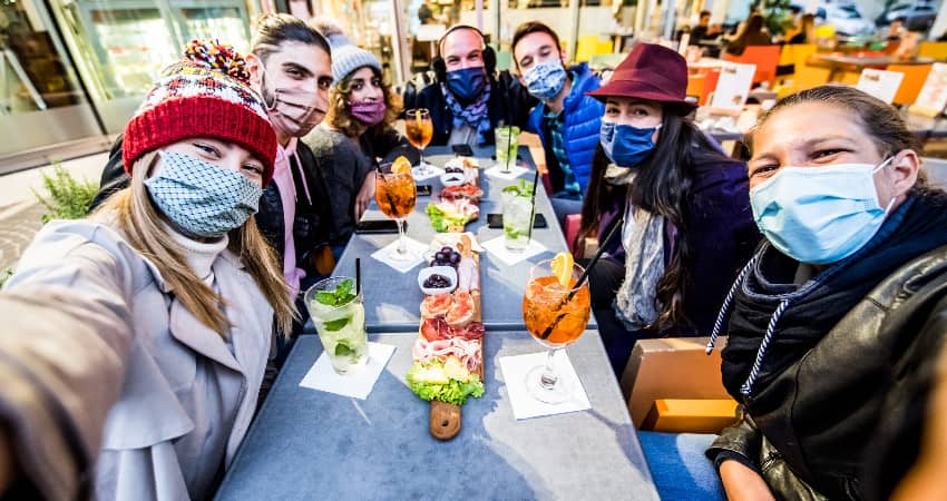 A group of dinner guests in masks enjoy appetizers in an outdoor restaurant