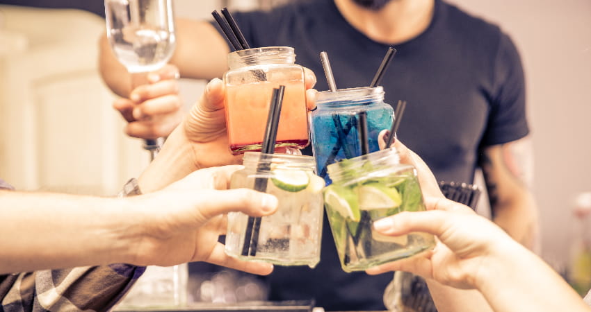 Glasses containing brightly colored coktails are toasted in an airy bar