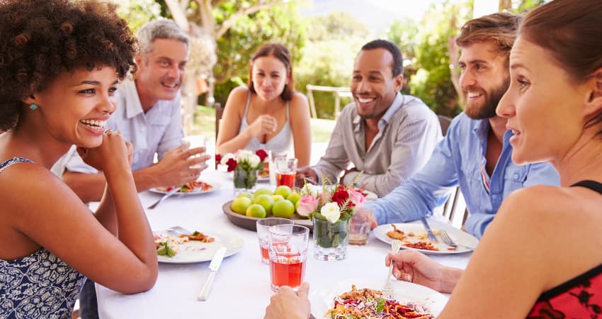 A large group of diners eat at an outdoor table on a sunny day