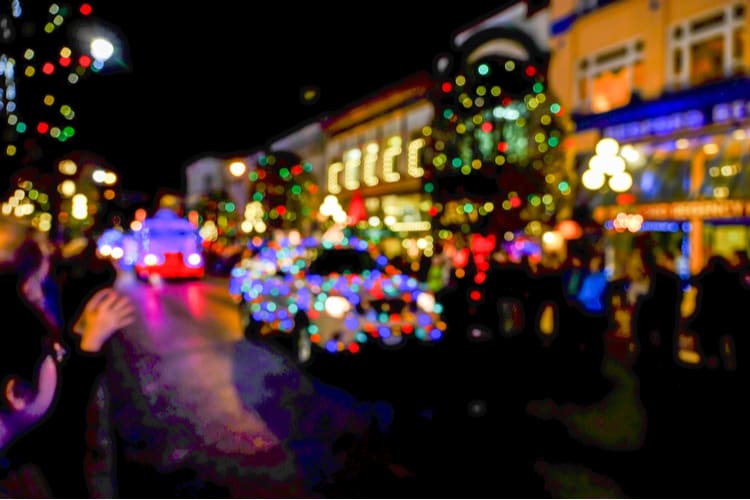 a blurred image of a car with holiday lights going down a street with lots of colorful light displays