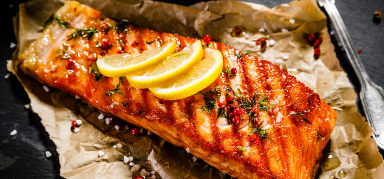 a fresh piece of grilled salmon with seasonings and lemon slices on top