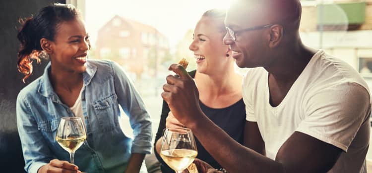 friends smile while gathered around a table with food