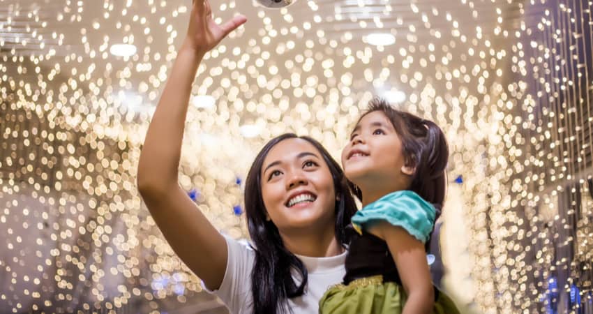 A woman holding a child while walking under glittering lights 