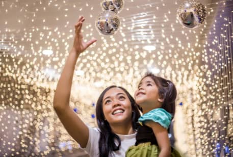 A woman holding a child while walking under glittering lights