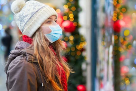 a woman with a beanie hat and facemask looks at a holiday store display in a window