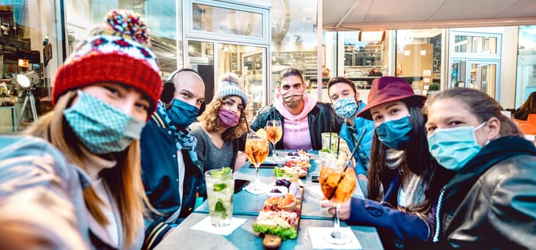 a family smiles for a selfie while wearing face masks at a table