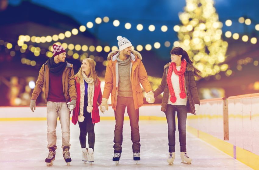 group of four friends holding hands and ice skating with a christmas tree in the background