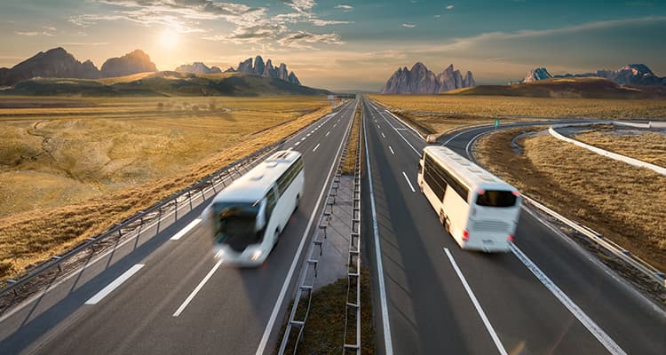 Two white charter buses driving on a road 