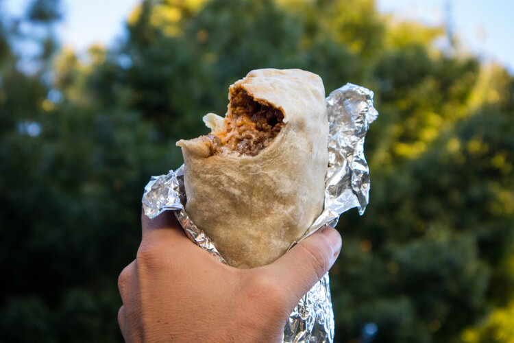 a burrito with a bite taken out of it with trees in the background