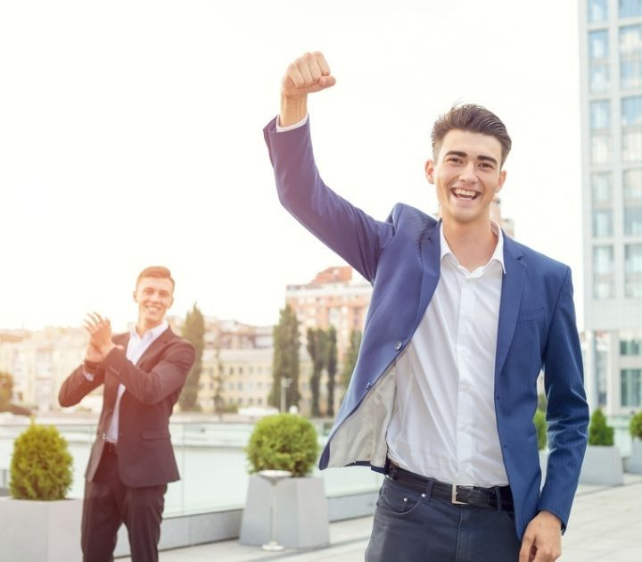 Man celebrating success with a fist in the air and a man clapping for him